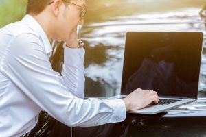 young businessman using laptop beside his car in a natural park