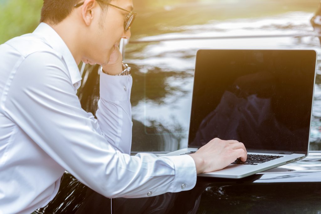 young businessman using laptop beside his car in a natural park